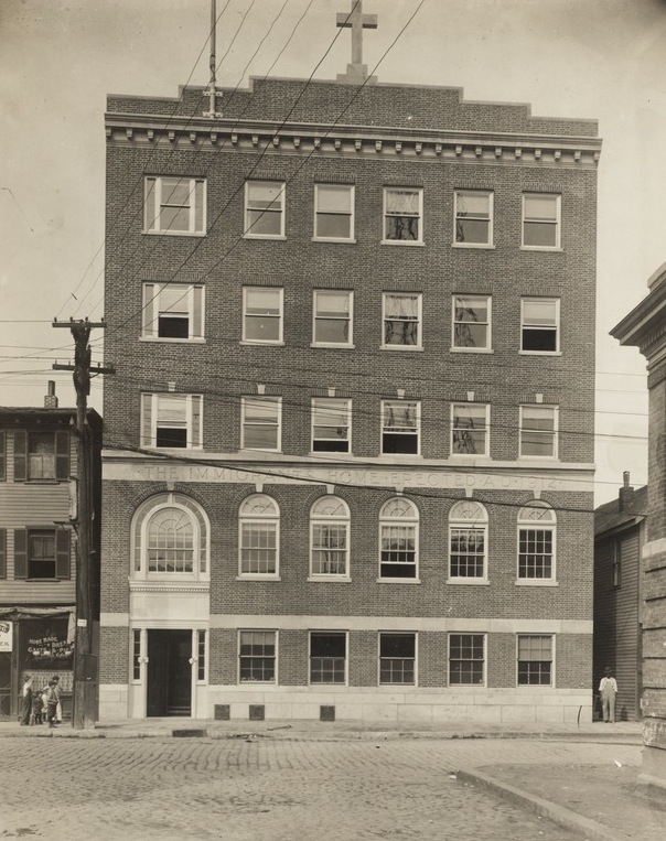 A five-story brick building with the words "The Immigrant Home: Erected AD 1812" in between the second and third floors.