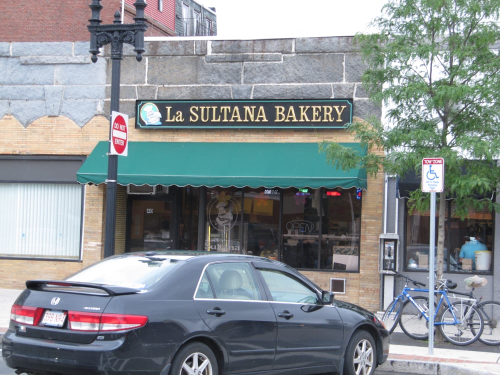 A photograph of a business with a large awning out front and a sign that reads "La Sultana Bakery." There is a car and two bikes outside of the building.