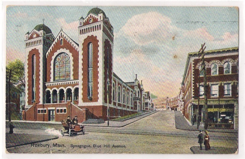 A postcard of "Roxbury, Mass. Synagogue, Blue Hill Avenue. The brick synagogue with a stained glass window is an intersection. A family rides by in an early automobile. Across the street from the synagogue is a drug store.