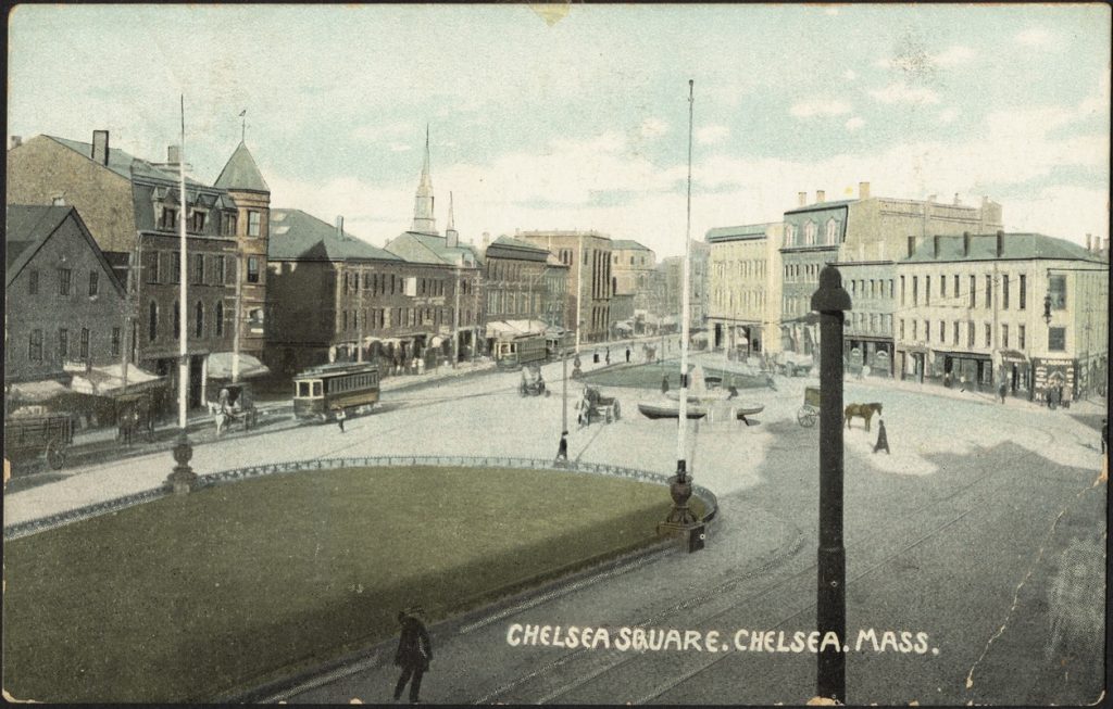 A postcard that depicts "Chelsea Square. Chelsea. Mass." A parkway with streetcars, horse drawn carriages, and pedestrians walking about. The road is in a U-shape and there are large three and four story buildings that mark the sides of the streets.