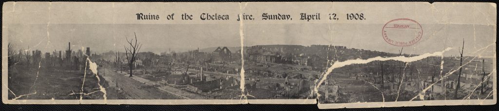 A wide photograph that shows the ruins from the Chelsea fire. On the left is land that is completely razed and towards the center and right, one can see the remnants of buildings that burned down. Throughout the photo are the trunks and remaining branches of trees that had burned down.