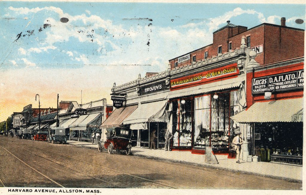 A postcard of "Harvard Avenue, Allston, Mass." There is a street on the left of the postcard with lines for a streetcar. On the side of the street are numerous businesses, such as a ten cent store, candy store, and cafe, along with automobiles.