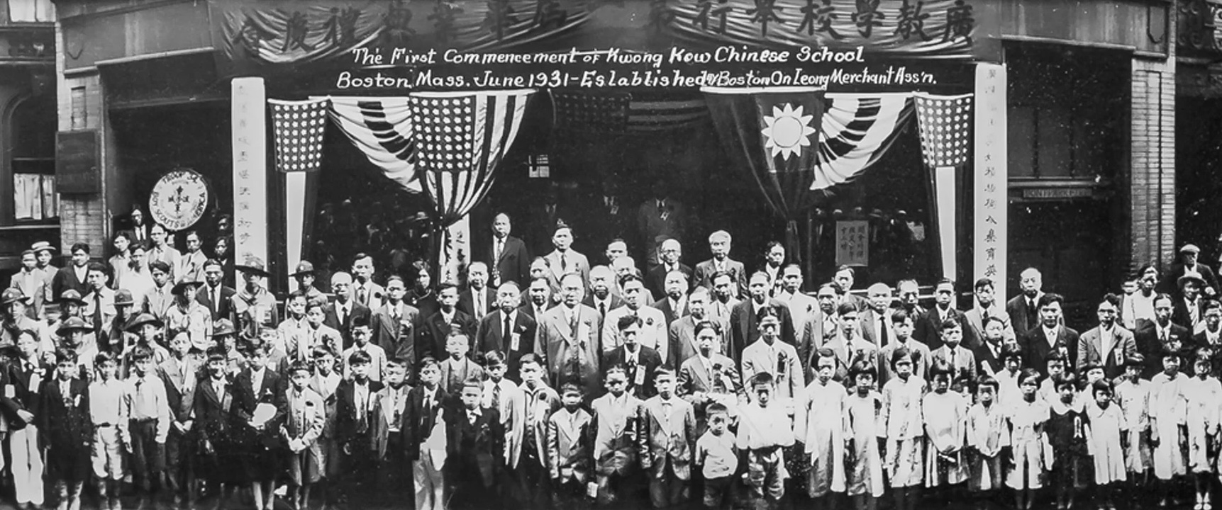 Several dozen students posed for graduation picture in front of the school with Chinese and American flag banners above.