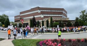 Dozens of protesters crossing street and surrounding ICE office in non-descript modern office building.